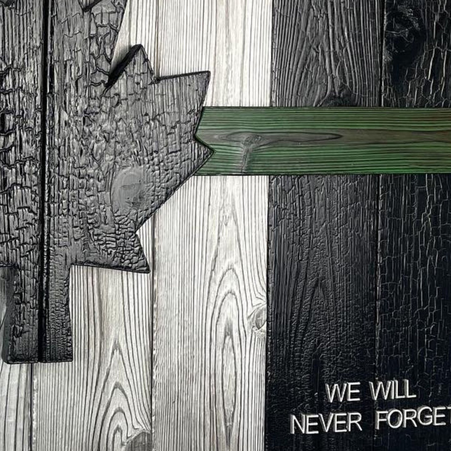 A handcrafted Canadian military flag made using the Shou Sugi Ban technique, giving the wood a rich, charred finish. The flag features a green thin line running horizontally across the design, symbolizing support for the military. The maple leaf emblem stands out against the dark, burned wood, highlighting the craftsmanship and depth of the texture.