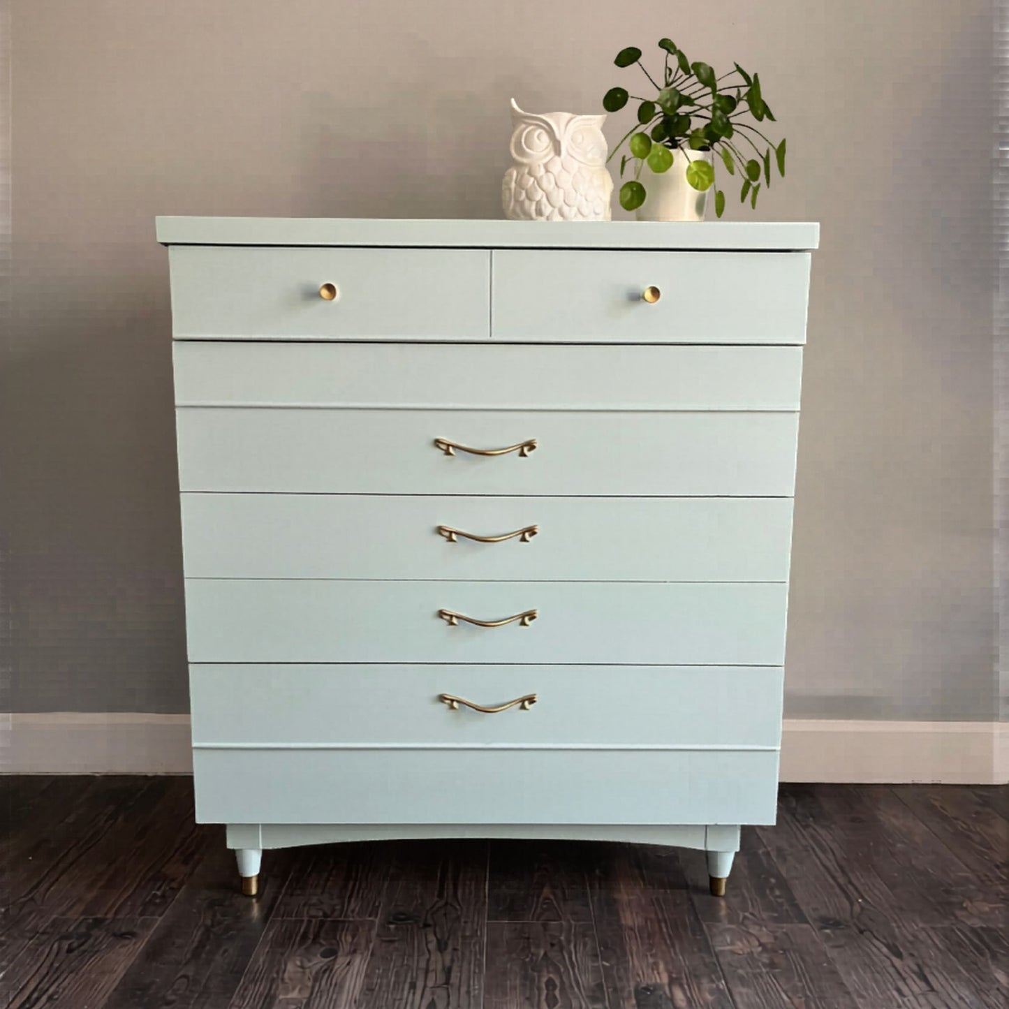 Light blue dresser with gold handles on a wooden floor against a neutral wall.
