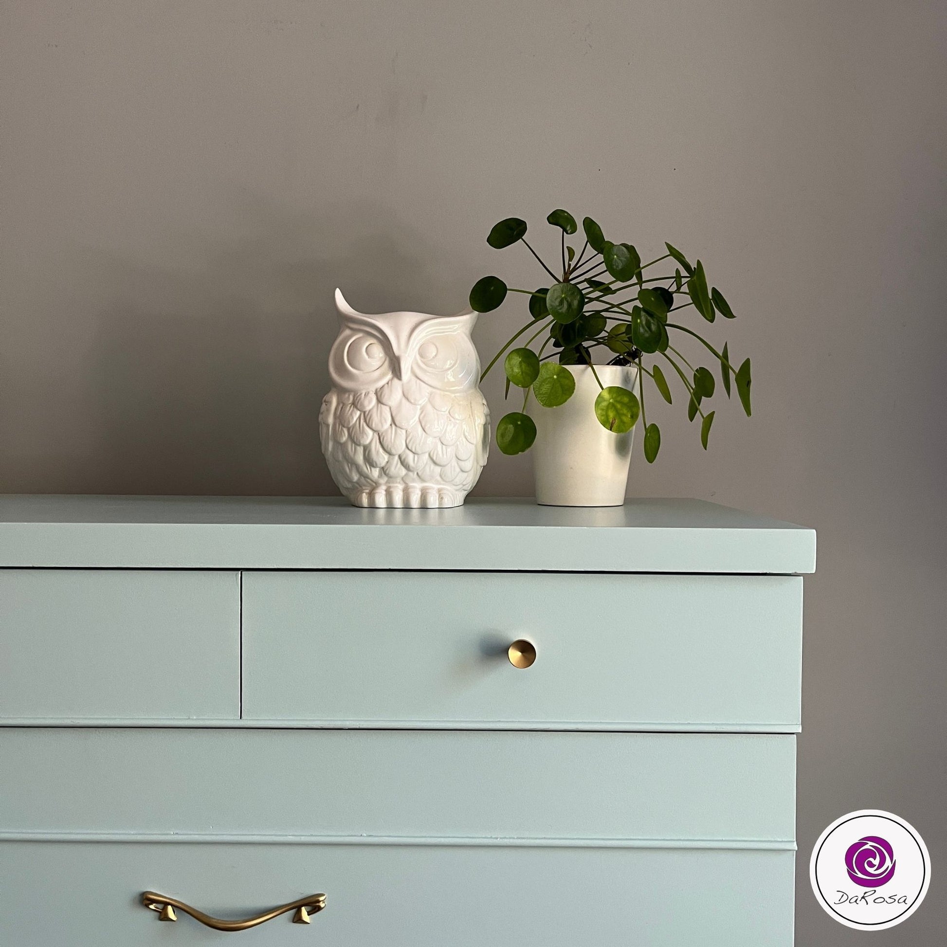 Light blue dresser with a white owl figurine and green plant on top against a gray wall.