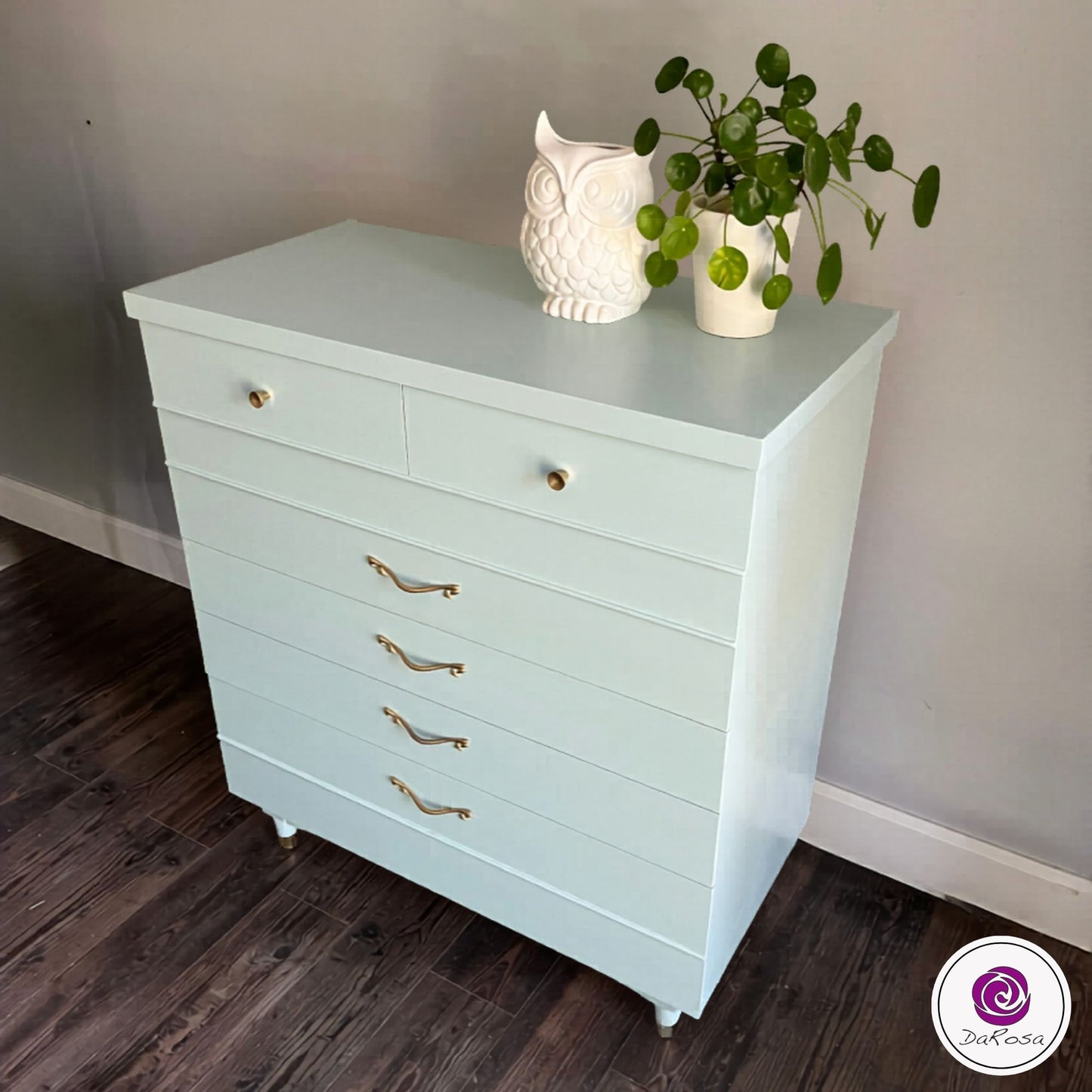 Light blue dresser with gold handles on a wooden floor against a gray wall.